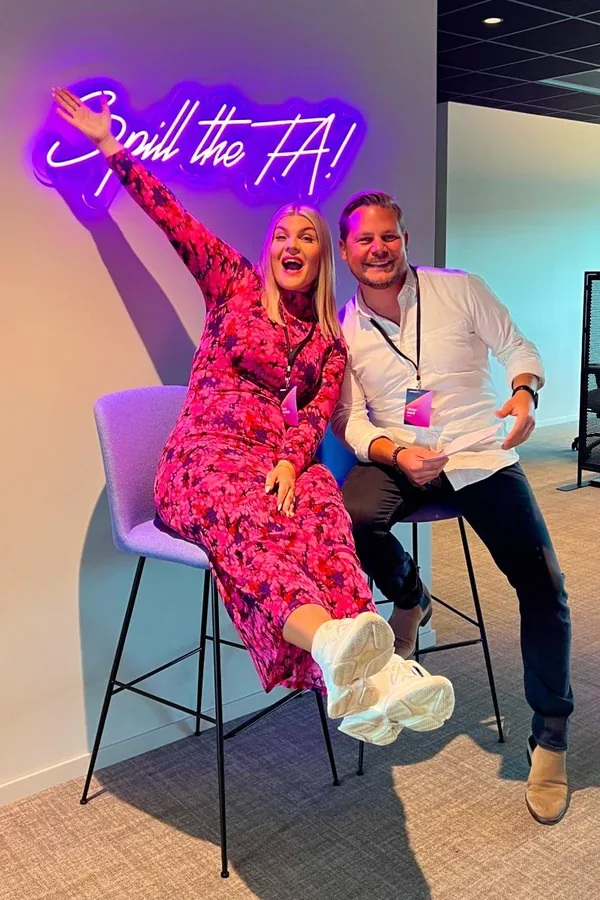 Two Adway colleagues having fun under the 'Spill the TA' neon sign